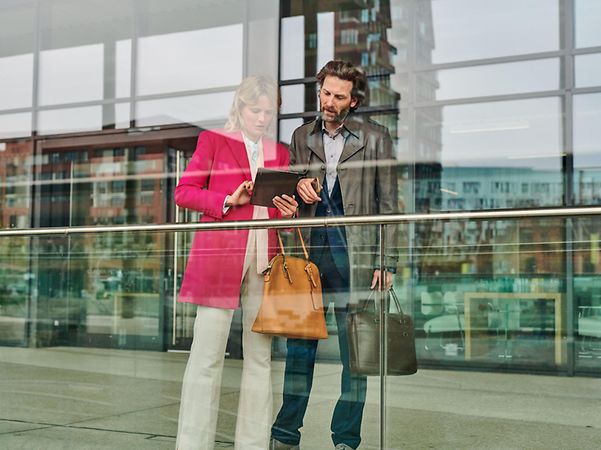 Mann und Frau schauen vor Bürogebäude auf Tablet