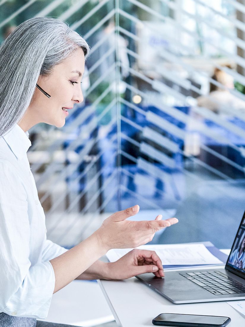 Eine Frau telefoniert vorm Laptop via Headset und informiert über Microsoft Dynamics 365