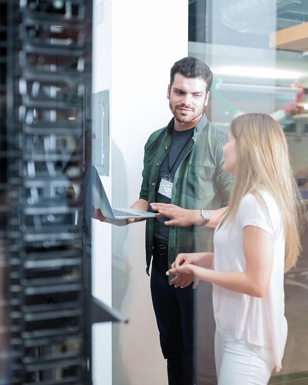 Zwei Personen unterhalten sich vor einem großen Serverschrank über das Managed IT-Portfolio der Telekom