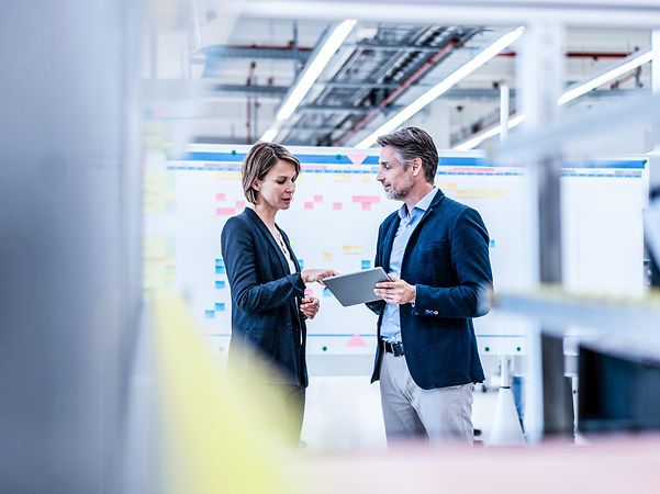 Geschäftsfrau und Geschäftsmann unterhalten sich in einer Fabrikhalle