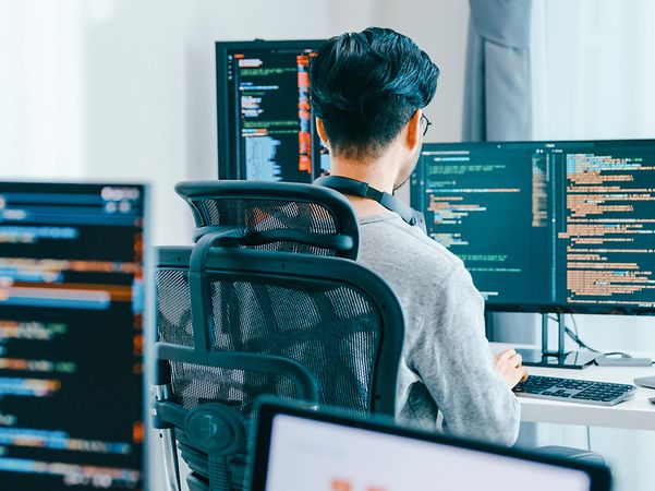 Blick über die Schulter eines Entwicklers auf Computerbildschirme mit Codezeilen.