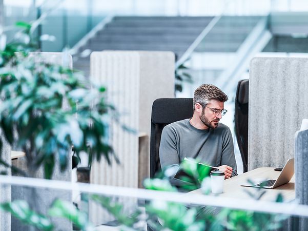 Ein Mann sitzt im Büro und schaut auf seinen Laptop.
