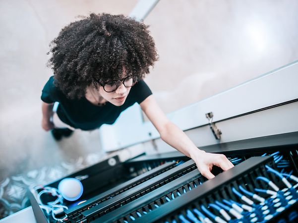 Eine junge Frau steht vor einem Netzwerkserver-Panel und prüft ein Kabel