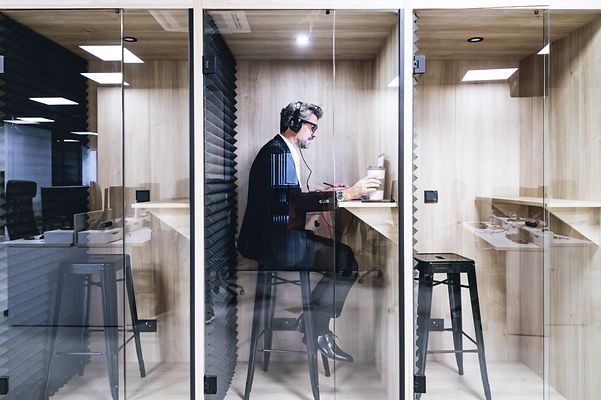 Eine Führungskraft in einer schalldichten Kabine, mit Kopfhörern, ist in die Arbeit vertieft in einem modernen Büro