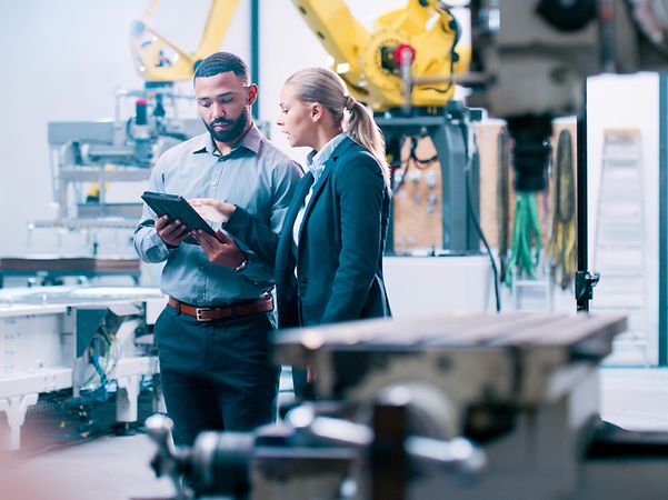 Zwei Ingenieure stehen in einer modernen Fertigungsanlage bei einer Besprechung am Tablet