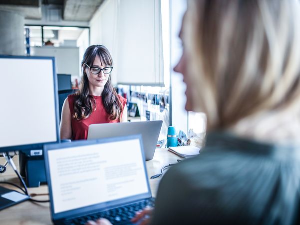 Zwei Frauen arbeiten in einem Büro digital zusammen.