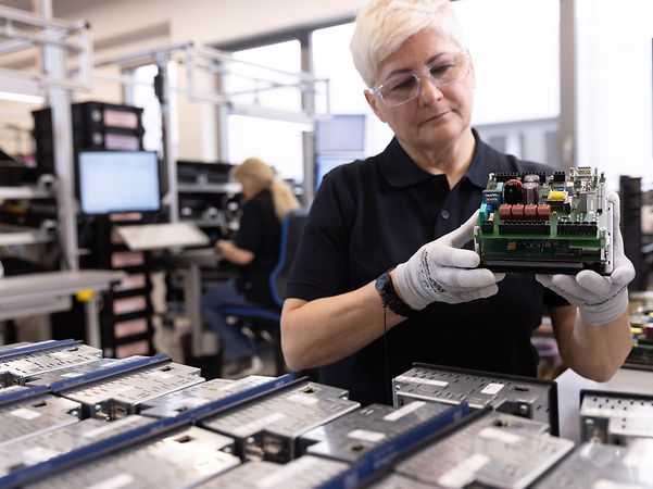 Janitza - Produktionsmitarbeiterin mit Schutzbrille und Handschuhen bei der Messgeraete-Pruefung