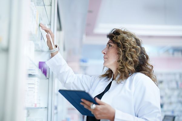 Telematik für Apotheken Eiene Apothekerin sucht mit Ihrem Tablet im Regal nach verfügbaren Medikamenten