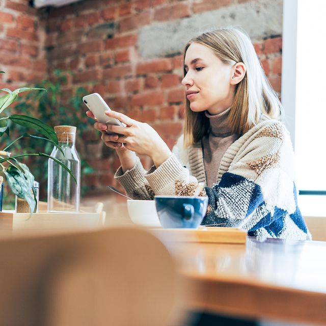 Junge Frau nutzt über das Smartphone Microsoft 365 beim Sitzen am Tisch