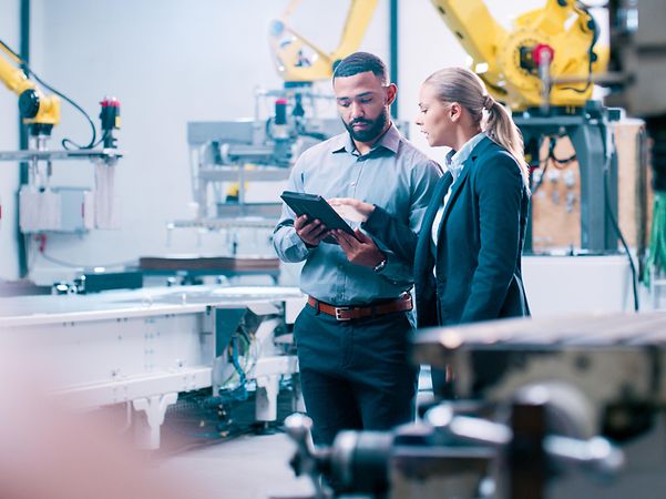 Zwei Ingenieure stehen in einer modernen Fertigungsanlage bei einer Besprechung am Tablet