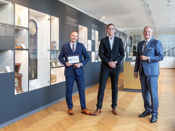 Junghans Uhren Vitrine und Herren in dunklen Anzuegen mit SAP-Tablet