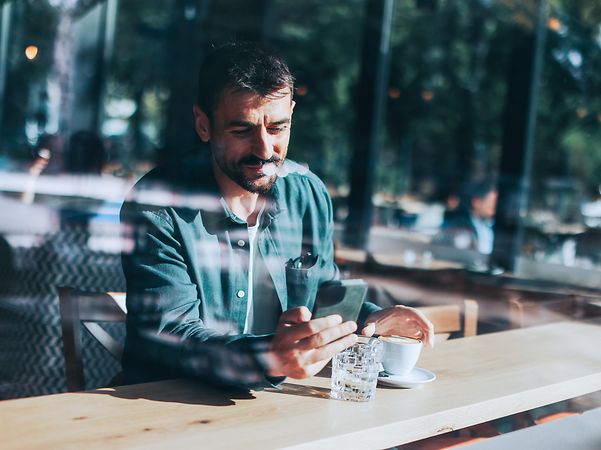 Ein Mann in einem Cafe liest eine Nachricht, die über SMS Massenversand gesendet wurde