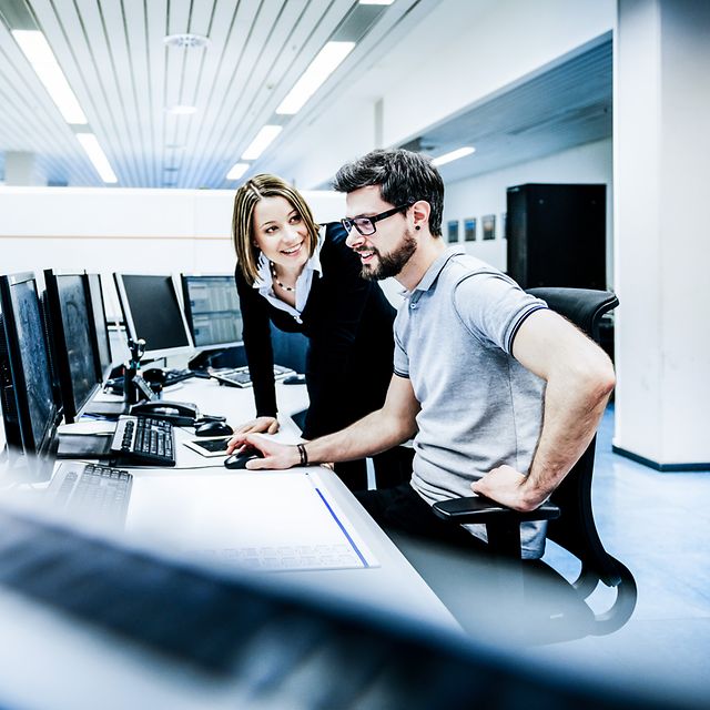 Eine Frau erklärt einen Mann etwas am Arbeitsplatz.