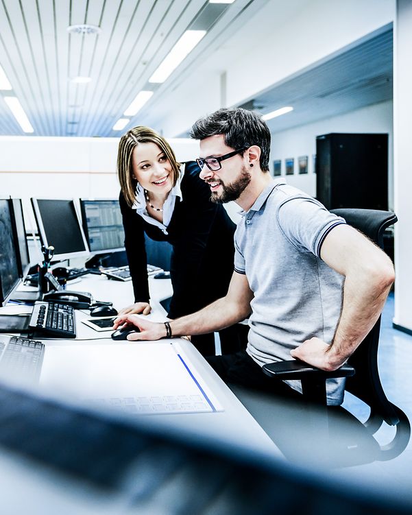 Eine Frau erklärt einen Mann etwas am Arbeitsplatz.
