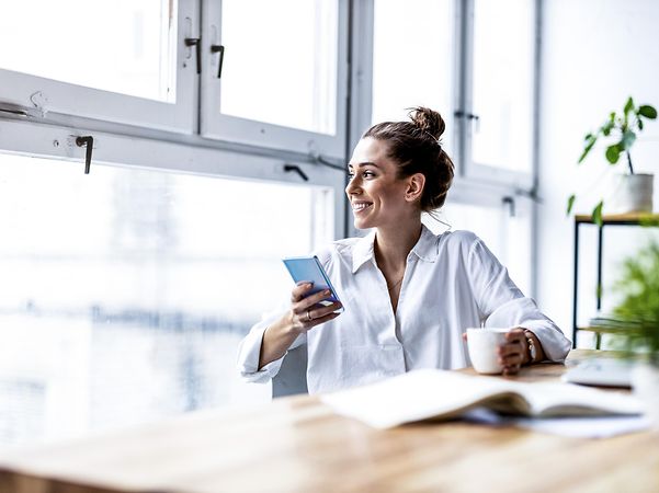 Frau schaut aus dem Fenster und hat ein iPhone in der Hand