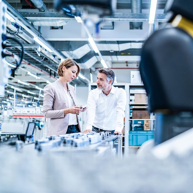 Zwei Personen in Businesskleidung sprechen in einer Werkshalle über digitale Lösungen der Telekom für Unternehmen