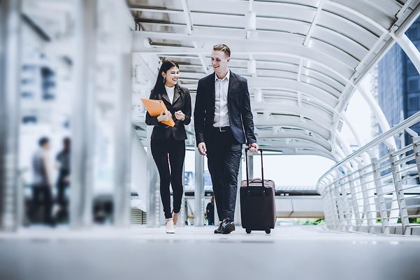 Zwei Businessleute mit Trolley unterhalten sich vor einem Hotel.