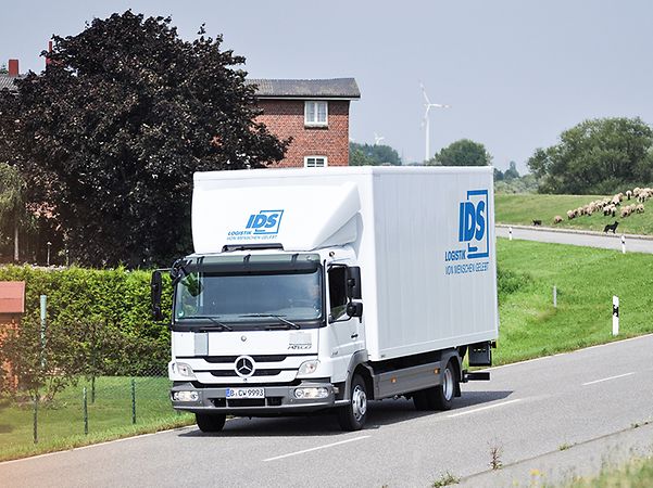 Weisser LKW von IDS Logistik auf einer Landstrasse in laendlicher Umgebung