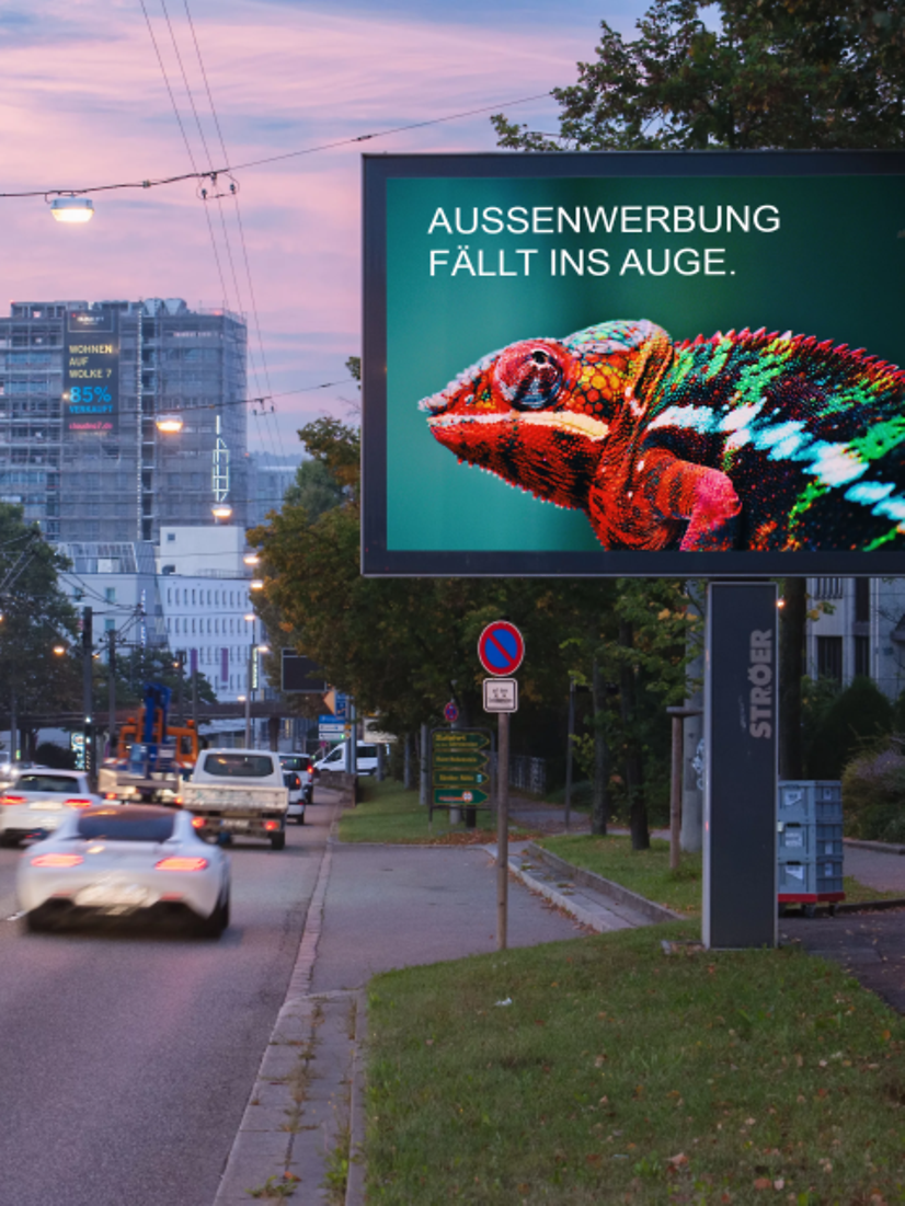 Bild zeigt ein beleuchtetes Citylight auf einer befahrenen Hauptstraße in Stuttgart während der frühen Abendstunden