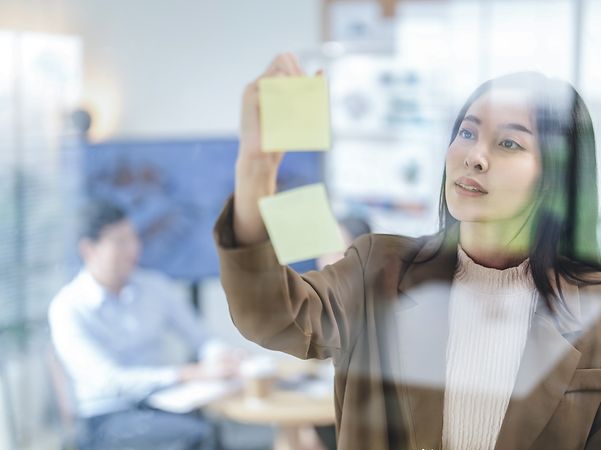 Eine Frau klebt ein Post-It an eine Glaswand