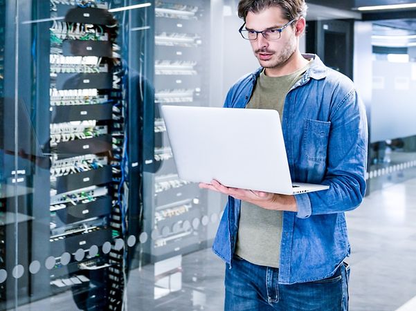 Ein Mann steht im Serverraum und schaut auf einen Computerbildschirm