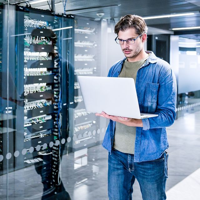Ein Mann steht im Serverraum und schaut auf einen Computerbildschirm