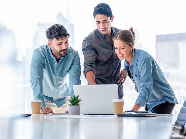 Drei Personen schauen auf einen Laptop-Bildschirm und besprechen ein Projekt.